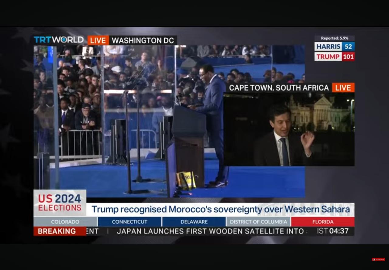 Live broadcast of a speaker at a podium in front of a large audience, with a live cross from Cape Town, South Africa